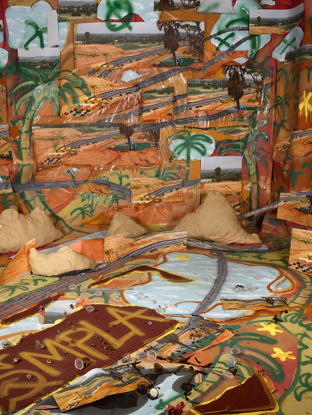 Collage backdrop of oil pipes among an orange and beige landscape and blue skies, with green spray-painted palms and x's drawn upon it. The foreground has a communist logo and "MPLA" spray-painted in yellow.