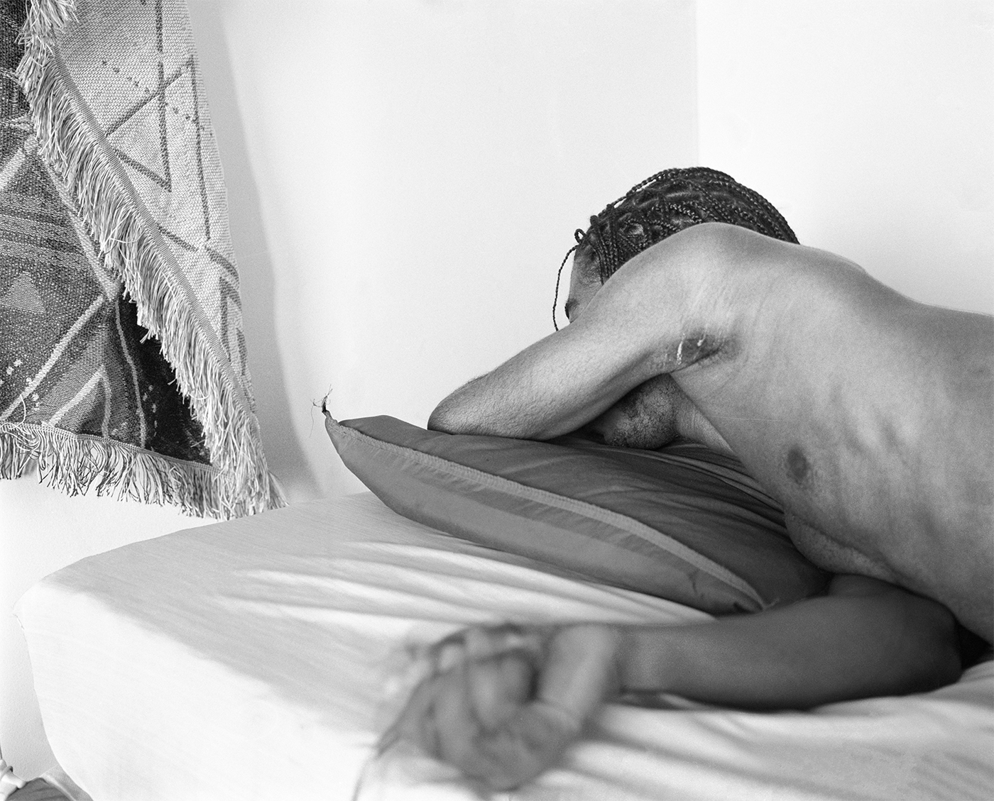 Photograph; a Black person lying on their side on a pillow with one arm covering their face and the other blurring into the foreground.