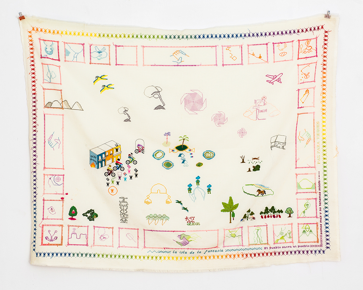 An embroidered map showing a small community settlement. Also includes symbols like shaking hands and other patterns in small, embroidered boxes framing the map.