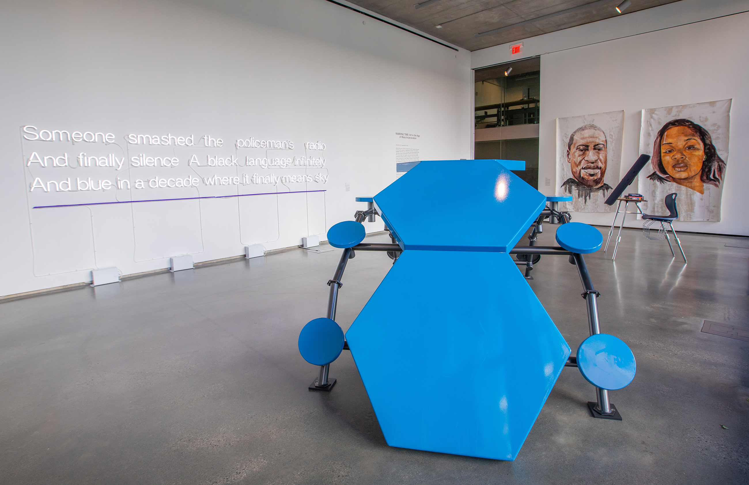 Gallery space with a bright blue sculpture in the foreground, and large-scale paintings of George Floyd and Breonna Taylor on one wall and illuminated text on another.